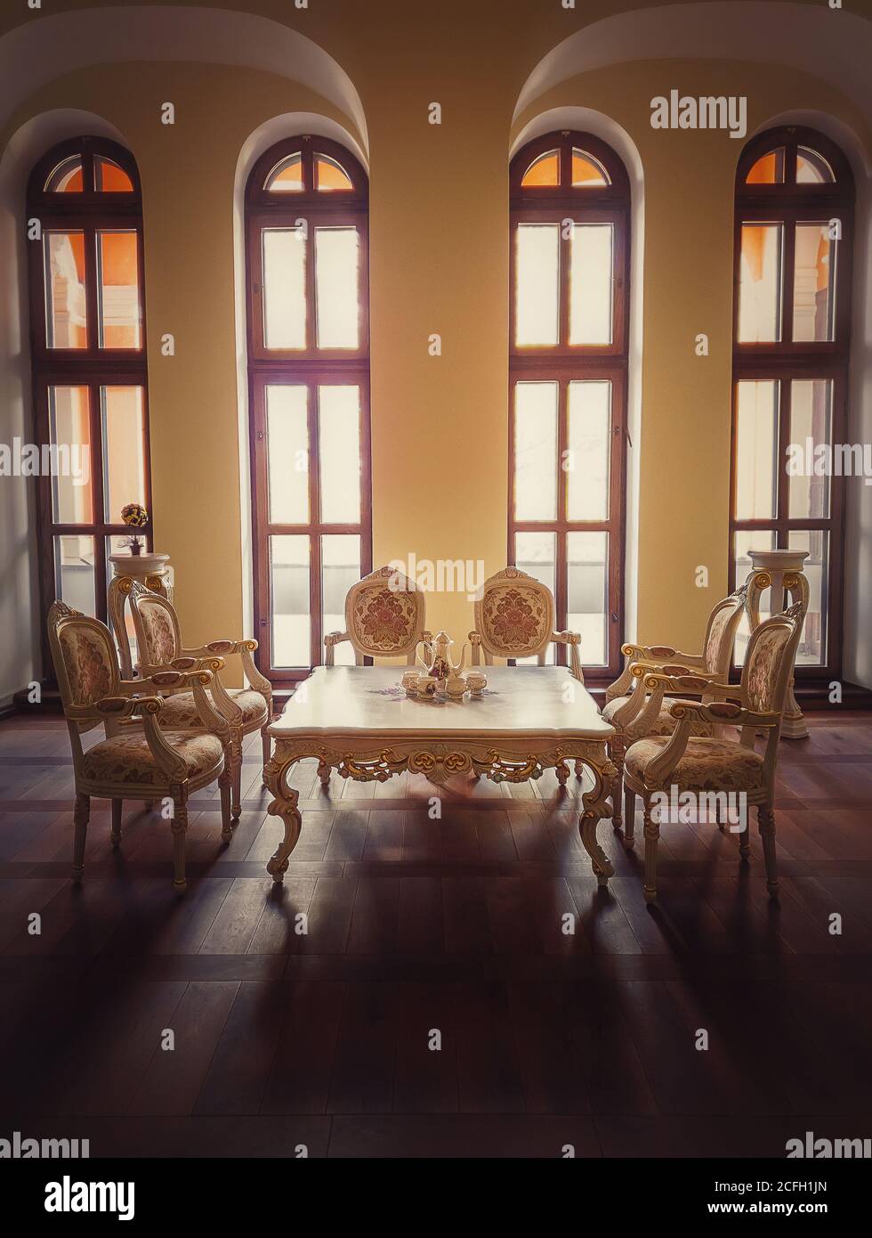 Antiguo comedor de la realeza, muebles de estilo medieval con sillas  adornadas de oro y mesa cerca de las ventanas arqueadas. Lujo de alojamiento  de fondo habitación, viejo Fotografía de stock -