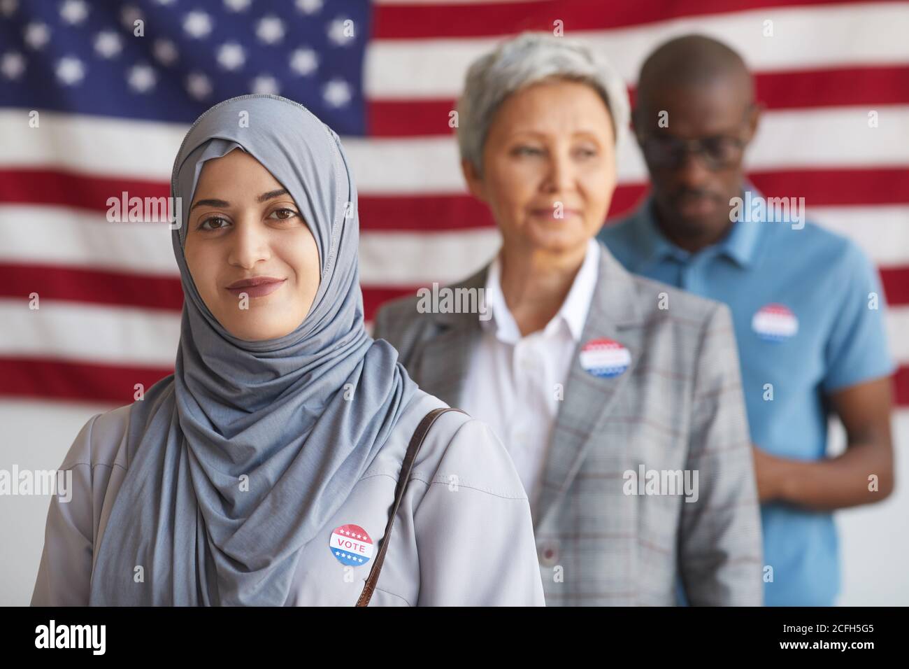 Grupo multiétnico de personas en la mesa de votación el día de las elecciones, se centran en la mujer árabe sonriente con HE VOTADO pegatina mirando la cámara, el espacio de copia Foto de stock