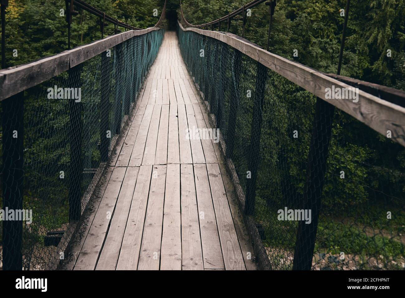 Vista del paisaje del puente colgante de acero largo. Viejo pequeño puente de madera a través del río sólo para peatones. Río de montaña rodeado de montañas y.. Foto de stock