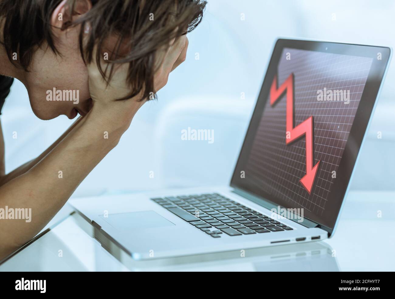 Triste hombre inversor de acciones perder dinero con las manos en la cara como la computadora portátil muestra un colapso del mercado financiero. Flecha roja económica hacia abajo. Foto de stock