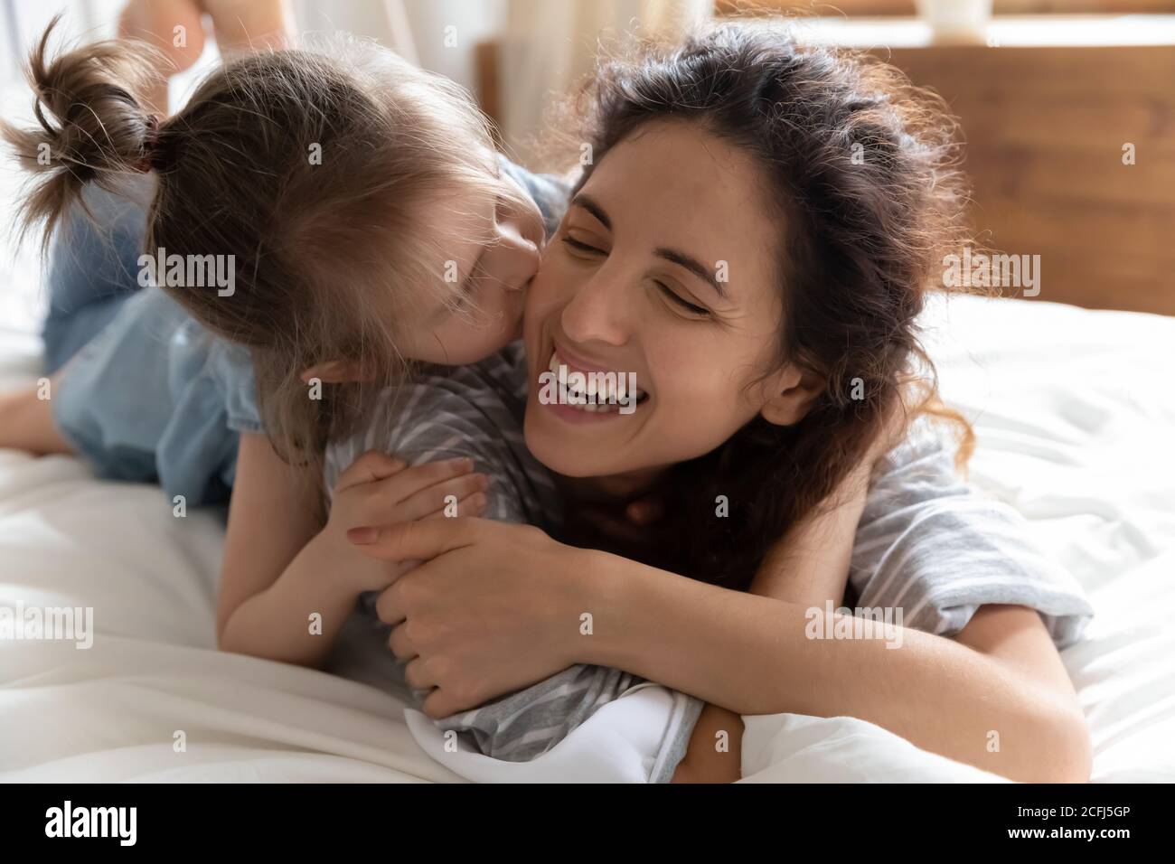 La hija besa la mejilla de la madre acostada en la cama se siente feliz Foto de stock