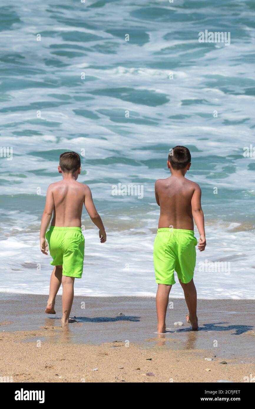 Dos niños pequeños en vacaciones de estatificación con vibrantes pantalones  cortos de color verde lima en Fistral Beach en Newquay, en Cornwall  Fotografía de stock - Alamy