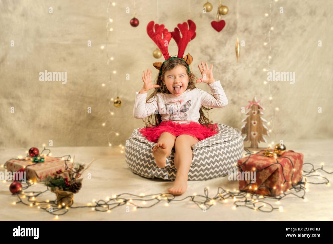 Sesión de estudio de Navidad de una linda niña con cinta de pelo de reno.  Fondo festivo, beige con regalos, bolas de Navidad y luces Fotografía de  stock - Alamy