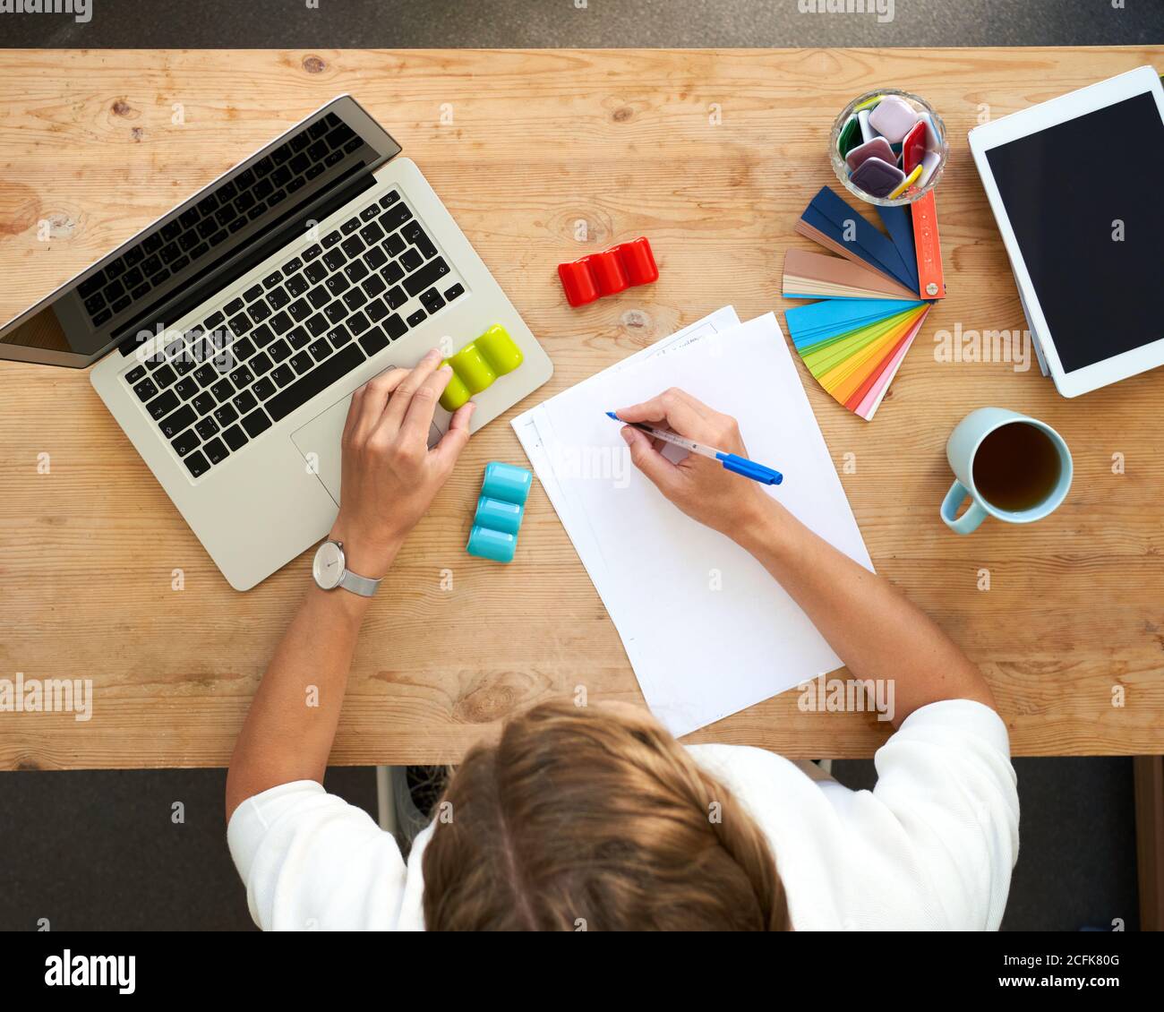 Lugar de trabajo de diseño, vista superior. Oficina en casa - escritorio con ordenador portátil, manos con juego de colores, selección de colores. Tableta digital y papel blanco para escribir Foto de stock