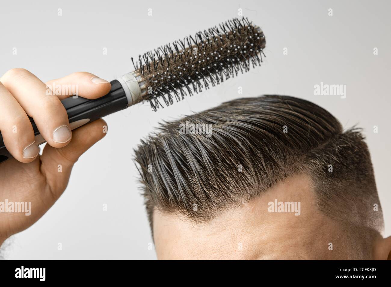 Hombre usando un cepillo redondo para moldear su cabello. Cuidado del  cabello en casa después de la peluquería. Peinado de pelo marrón corto  sobre el fondo blanco Fotografía de stock - Alamy