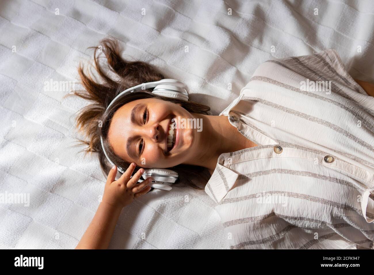 Niño de cosecha tocando los auriculares de la mujer acostada en la cama dormitorio y disfrutar escuchando música mientras mira una cámara Foto de stock