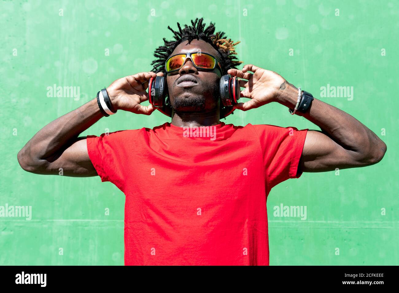 Atleta afroamericano masculino en ropa deportiva y con auriculares relajante en la calle después de entrenar en el día soleado mientras se está mirando Foto de stock