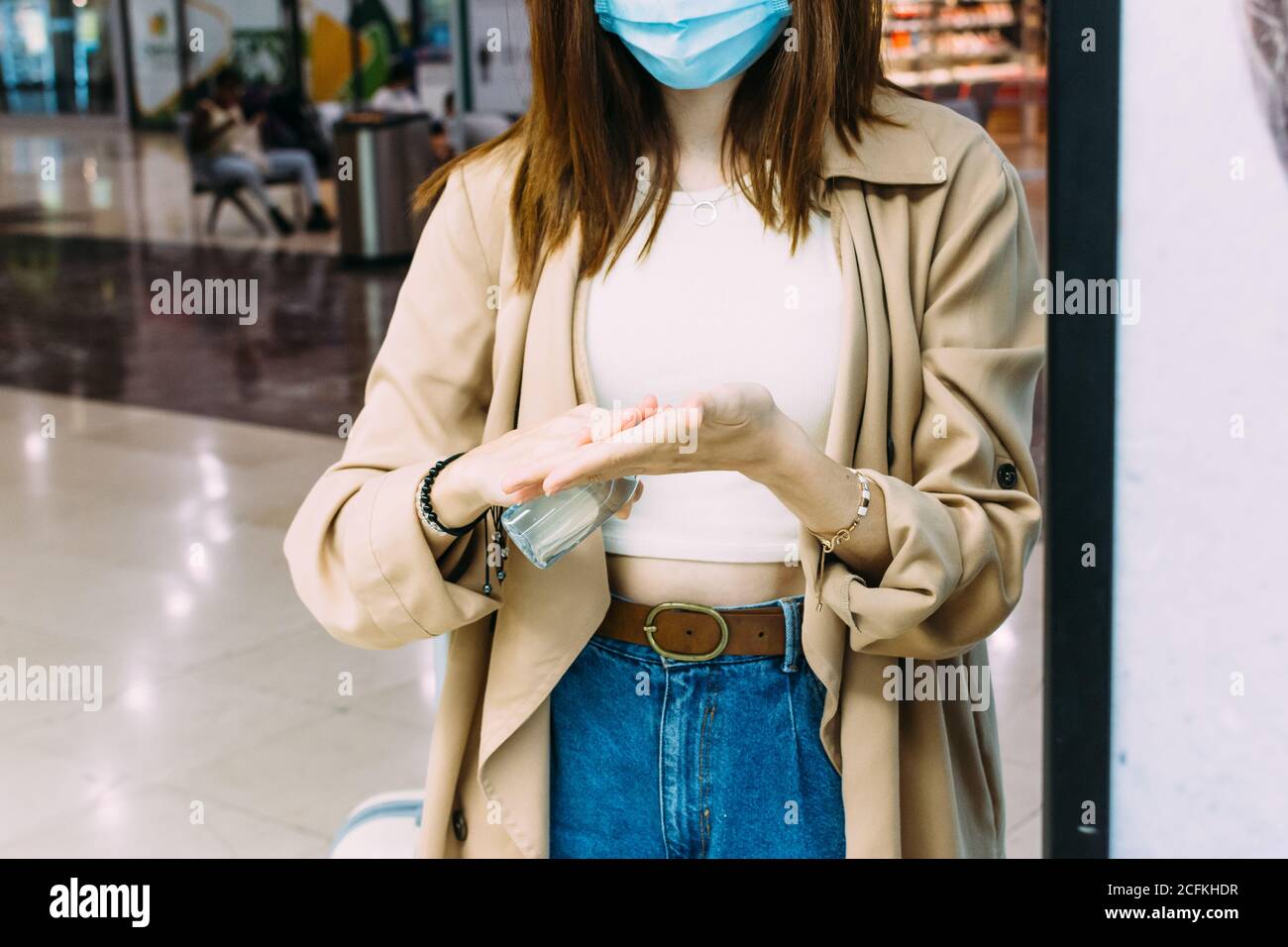 una mujer que lleva una máscara facial y usa gel hidroalcohólico para desinfectar sus manos en la estación de tren Foto de stock