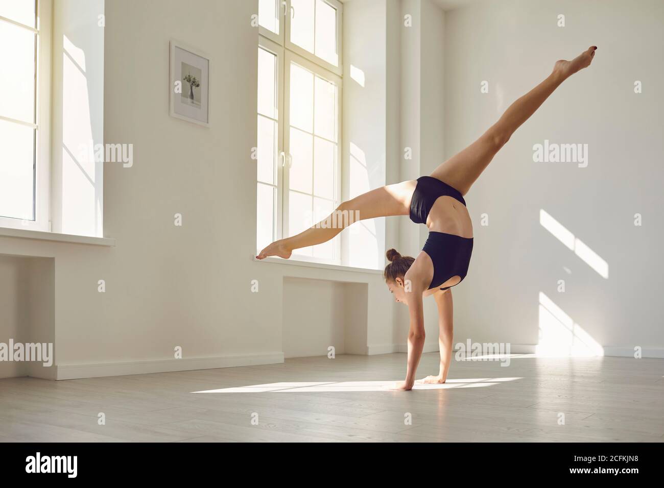 Gimnasia esbelta en sujetador deportivo top y shorts haciendo soporte de mano mientras practica gimnasia en el estudio Foto de stock