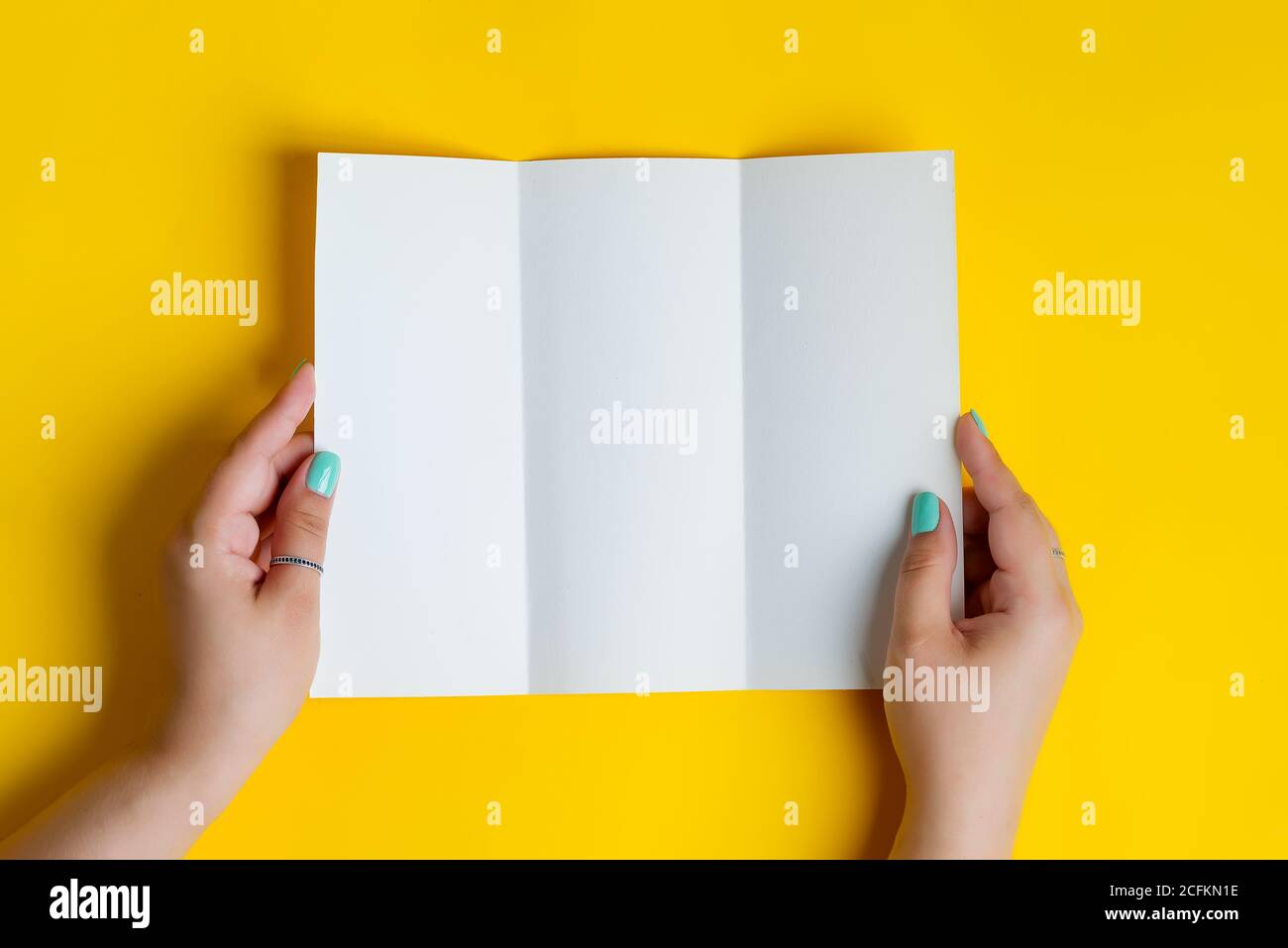 Folleto de tríptico de papel blanco en blanco folleto A4 en las manos de la  mujer sobre el fondo amarillo. Vista superior Fotografía de stock - Alamy
