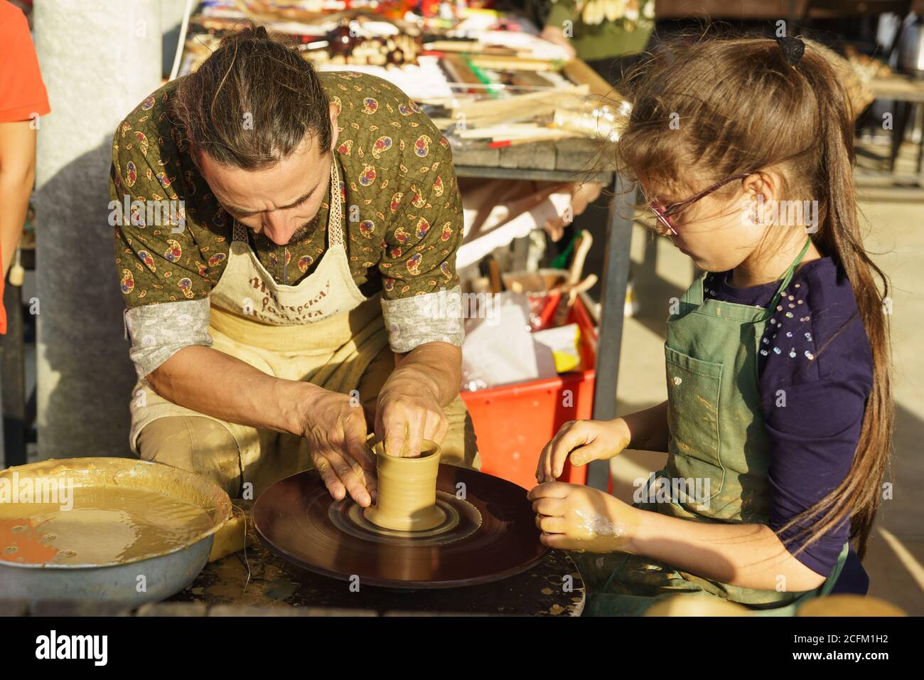 Moldavanskoye, Krymsk, Rusia-05 Octubre 2019: Un alfarero enseña a una chica a hacer una jarra de arcilla amarilla. Rueda de hilado de alfareros. Clase maestra en la f Foto de stock