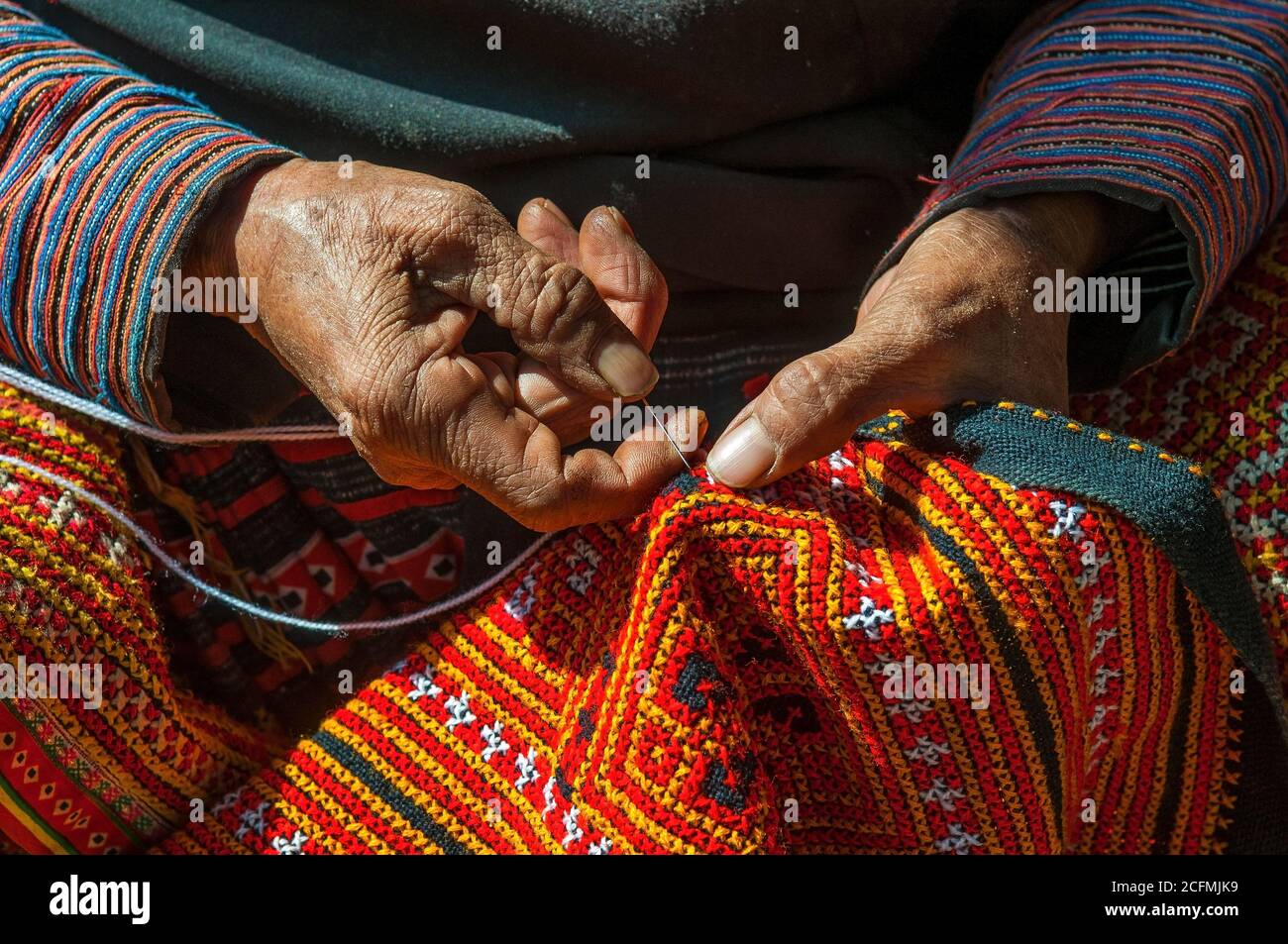Manos de una mujer Hmong negra cosiendo tela tradicional colorida y otras artes y artesanías con sus manos en la luz del sol, Vietnam del Norte. Foto de stock