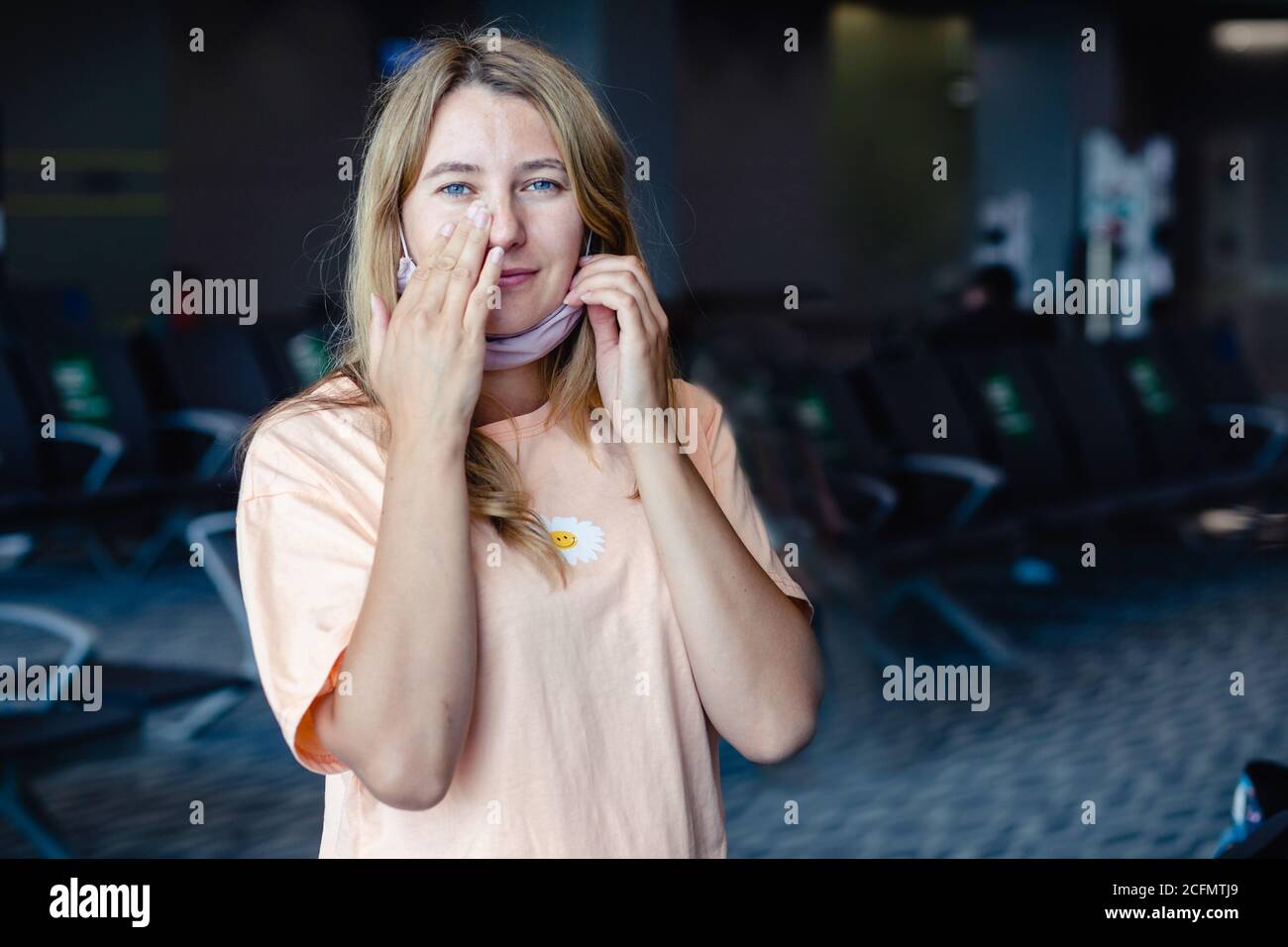 Chica que lleva una máscara de protección para coronavirus o covid 19 frotando su cara con las manos sucias en el aeropuerto. No toque su cara. Espacio de copia. Foto de stock