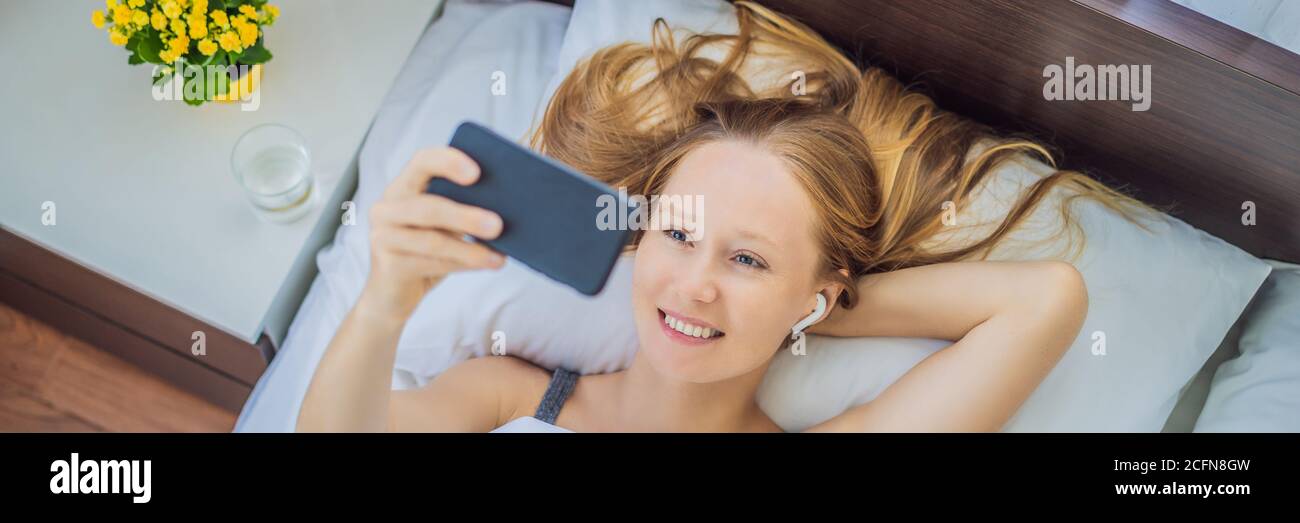 Mujer relajada usando un teléfono inteligente en la cama en la BANDERA de casa, DE FORMATO LARGO Foto de stock