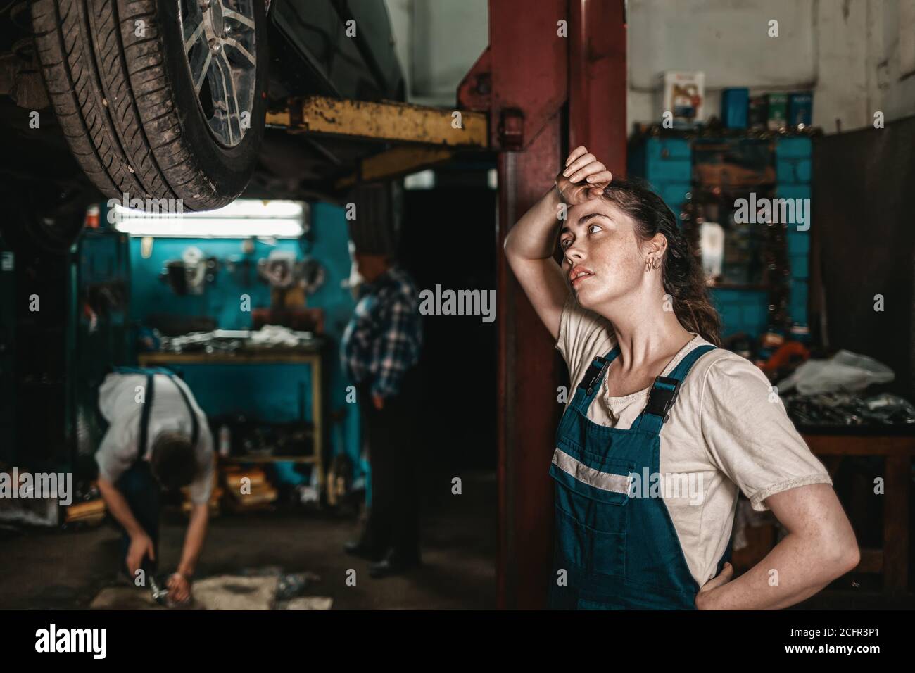 El concepto de la pequeña empresa, el feminismo y la igualdad de las mujeres. Una joven mecánica de automóviles se limpia wearily sudor de su frente. Foto de stock