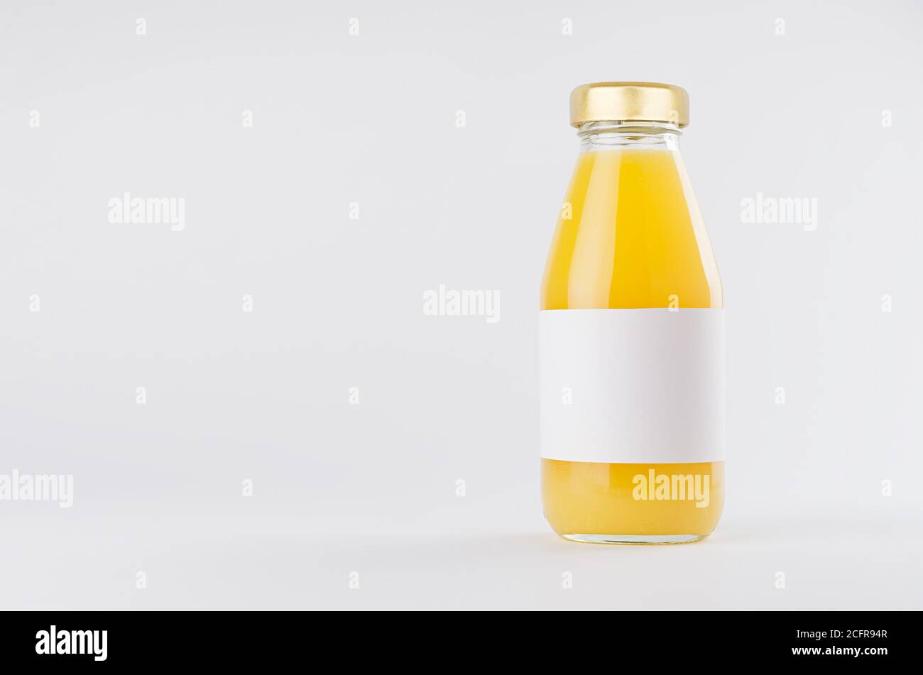 Jugo amarillo naranja en botella de vidrio con tapón de oro y blanco etiqueta en blanco se mofa sobre fondo blanco con espacio de copia, plantilla para el embalaje, advertisi Foto de stock