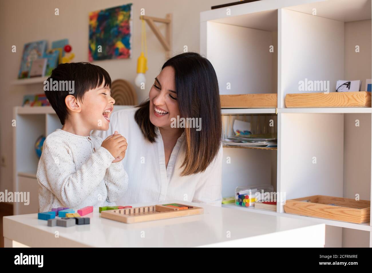 Lillte Kid jugando con un rompecabezas de madera de tetris y ayuda de madre o maestro. Resolución de problemas en casa. Comunidad de aprendizaje. Escuela Montessori Foto de stock
