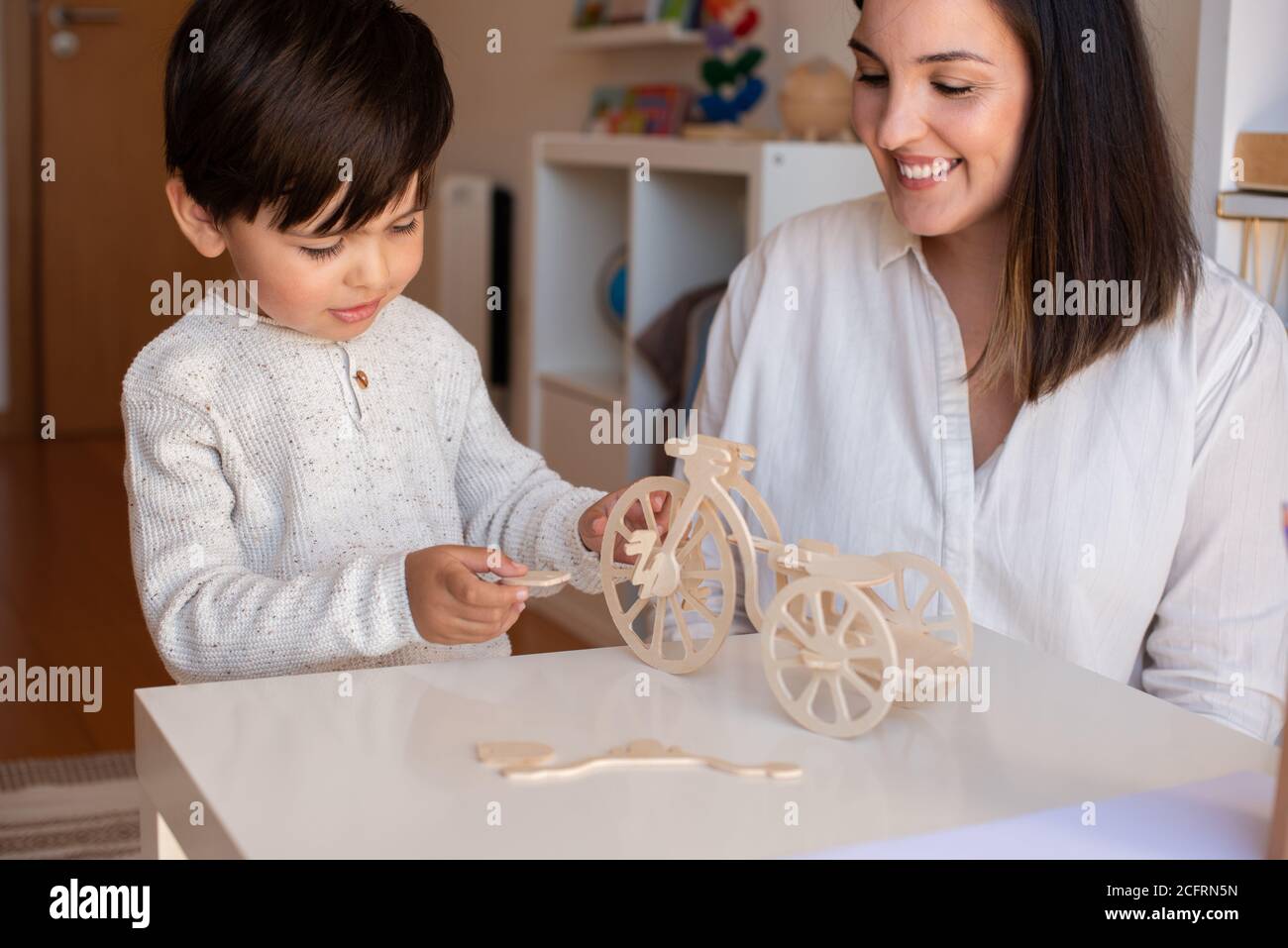 Liltle Preschooler Kid jugando con madera 3d rompecabezas y maestro educador ayuda. Resolución de problemas en casa. Comunidad de aprendizaje. Escuela Montessori Foto de stock