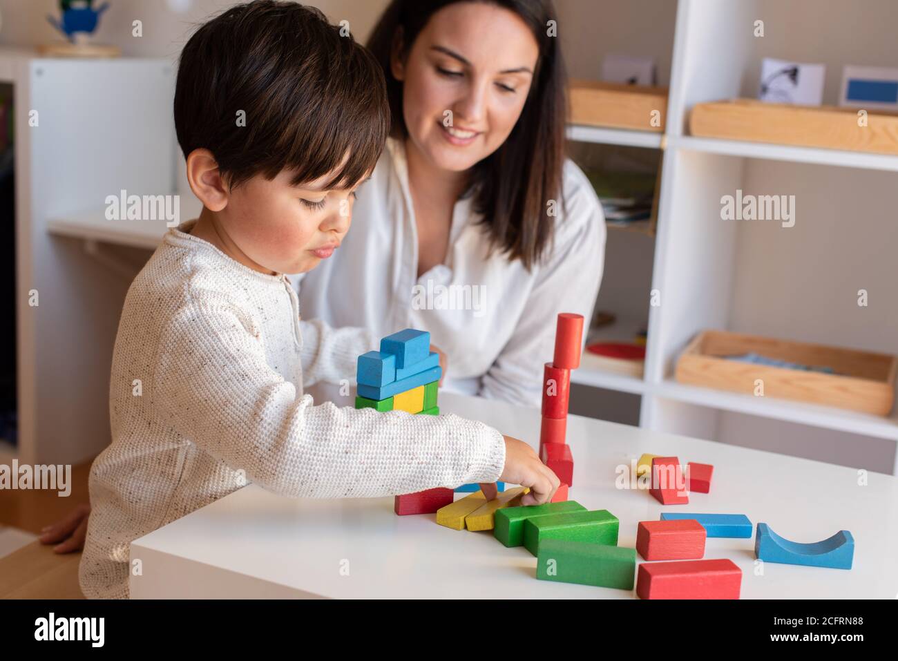 Liltle Preschooler Kid jugando con bloques de madera y la maestra educador ayuda. Resolución de problemas en casa. Comunidad de aprendizaje. Escuela Montessori Foto de stock