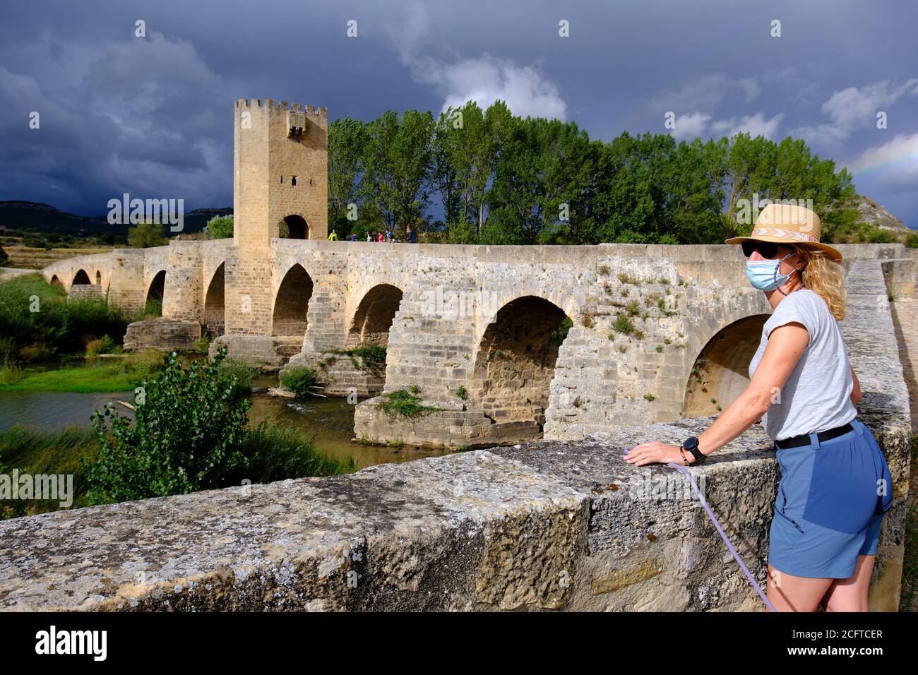 Mujer turística con un sombrero y una máscara y puente medieval y el río Ebro. Foto de stock