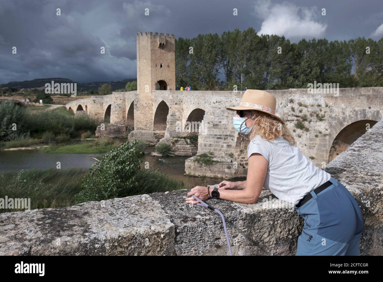 Mujer turística con un sombrero y una máscara y puente medieval y el río Ebro. Foto de stock