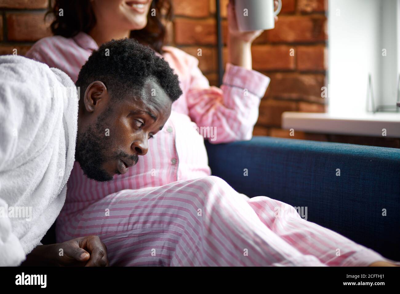 hermosa mujer embarazada y su guapo marido afro escuchando al bebé en el vientre, pasando tiempo juntos en casa Foto de stock