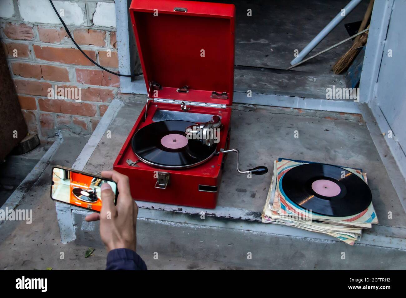 Viejo jugador de discos rojo vintage con discos de vinilo fuera de casa. Una mano de hombre graba en el móvil cómo se reproduce la música haciendo video. Estilo antiguo para escuchar mu Foto de stock