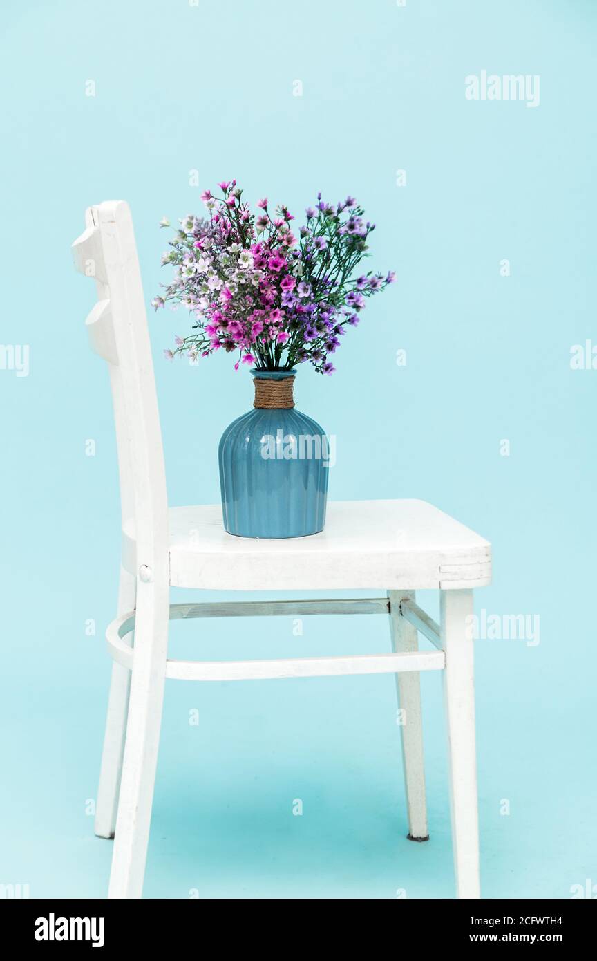 Ramo de flores de lavanda artificial en jarrón de cristal sobre silla blanca y fondo azul. Interior de estilo minimalista. Espacio de copia. Foto de stock