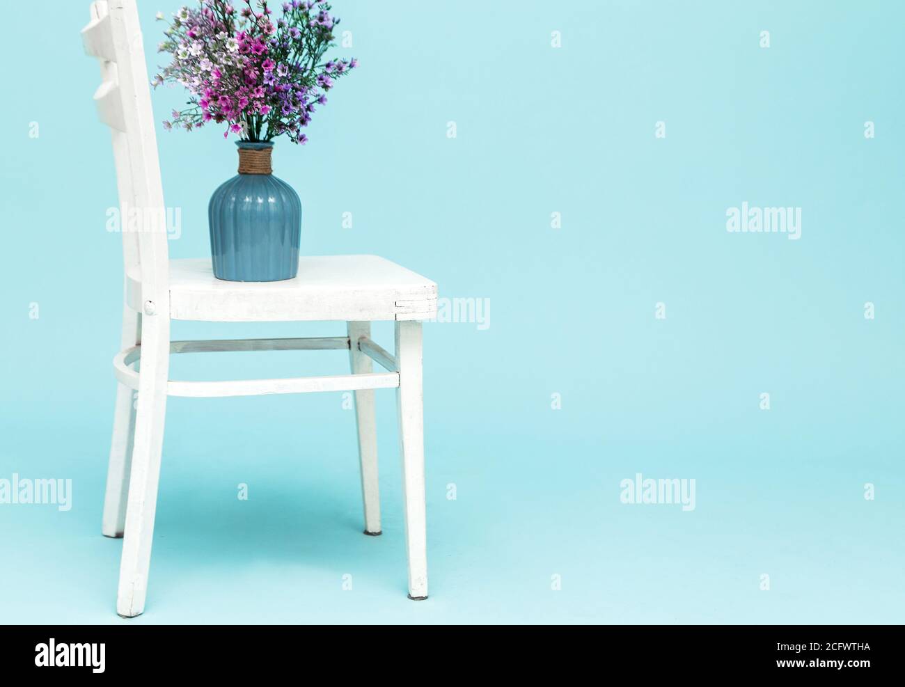 Ramo de flores de lavanda artificial en jarrón de cristal sobre silla blanca y fondo azul. Interior de estilo minimalista. Espacio de copia. Foto de stock