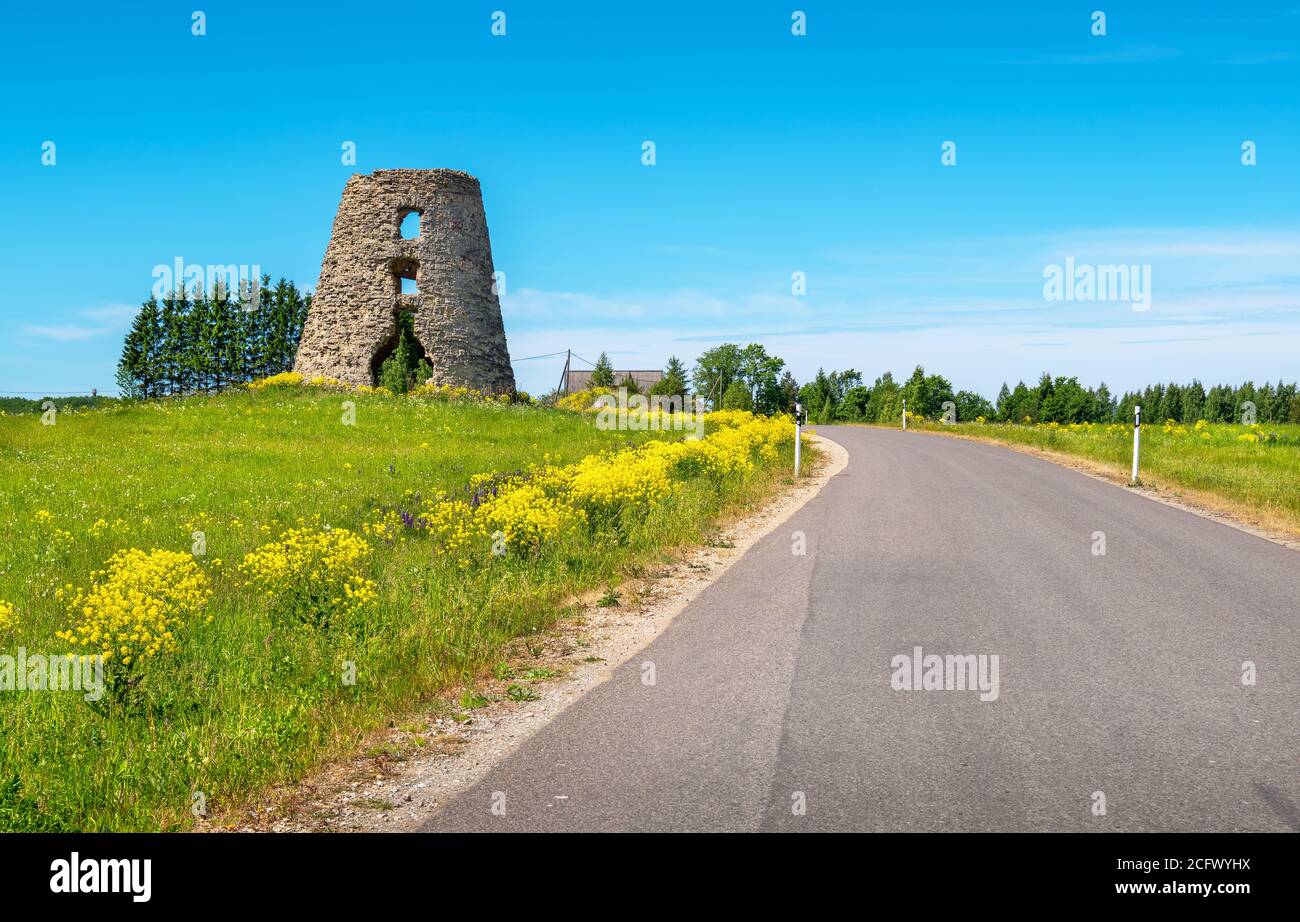 Paisaje rural con carretera y ruinas de un antiguo molino de viento. Estonia, Estados bálticos, Europa Foto de stock