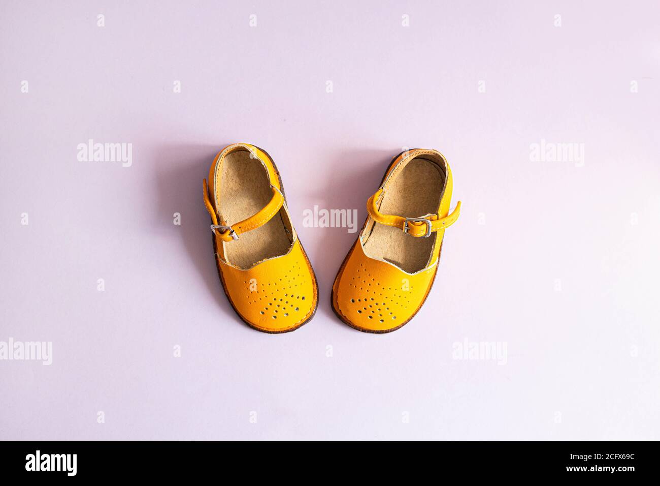 Zapatos bebé de color amarillo brillante sobre fondo lila con copyspace. Concepto de ropa para bebés. Vista superior, disposición plana Fotografía de stock -