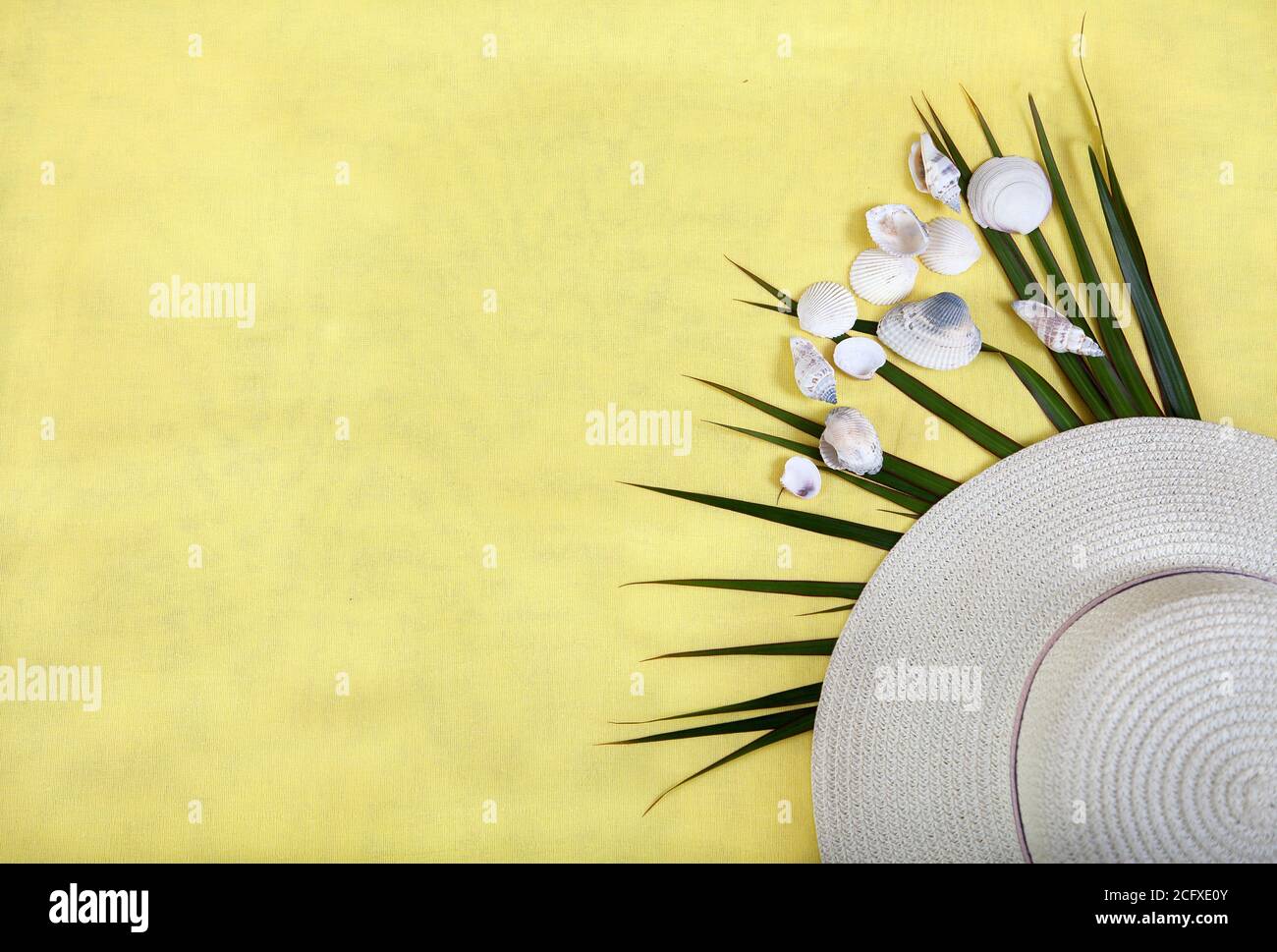 Sombrero de paja blanco y hojas de palma sobre un fondo amarillo. Concepto de vacaciones. Copiar espas. Lay plano Foto de stock