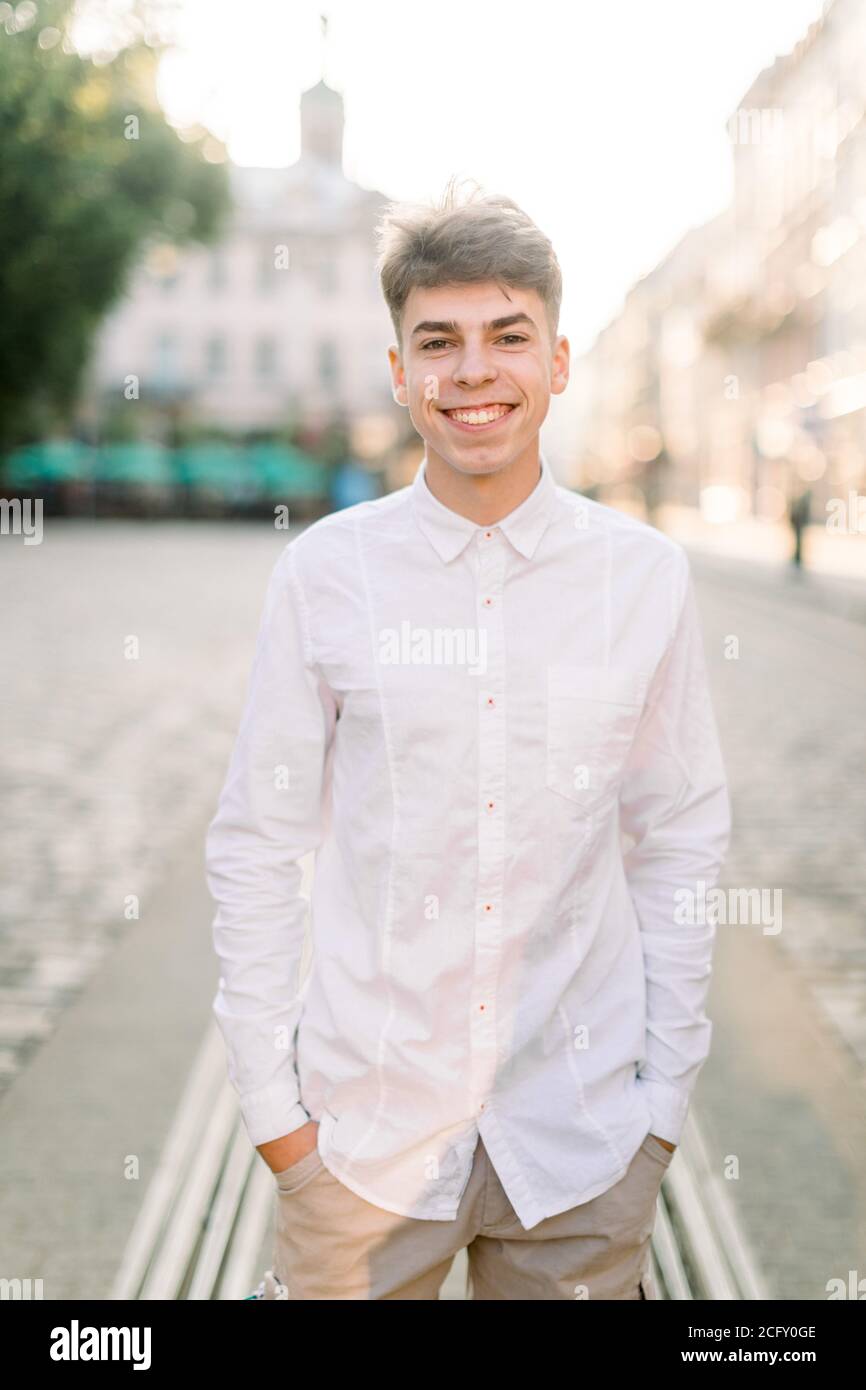 Joven hombre caucásico con estilo con camisa blanca y pantalones beige, de  pie en la calle sobre el fondo de la hermosa ciudad antigua europea,  sonriendo Fotografía de stock - Alamy