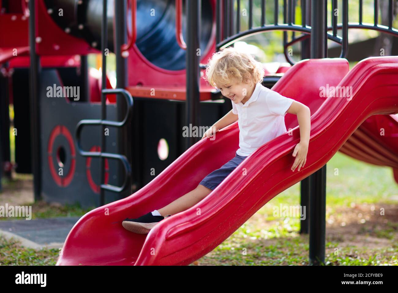 Niños jugando en un patio exterior. Los niños juegan en el patio de la escuela o guardería. Active kid sobre diapositivas coloridas y swing. Actividad de verano saludable para chi Foto de stock