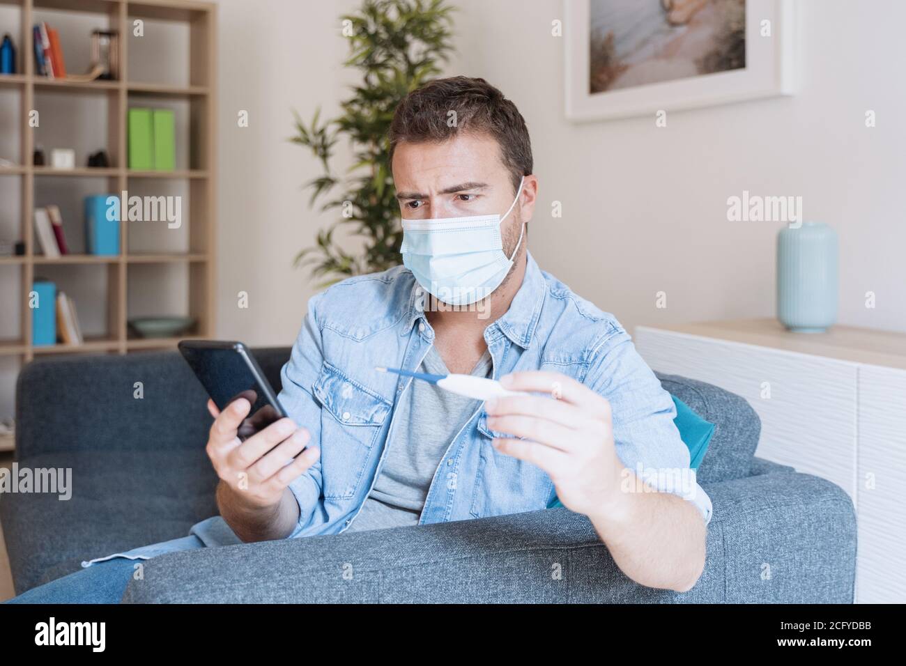 Hombre con síntomas de gripe revisar la temperatura y llamar a un médico Foto de stock