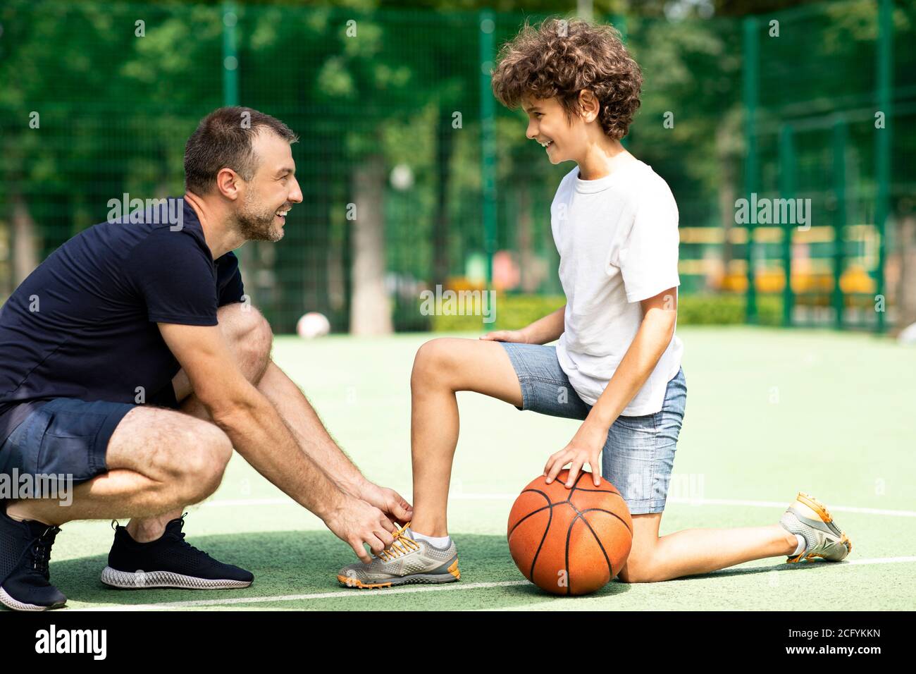 Hombre sonriente atando los cordones de niño rizado en el campo Foto de stock