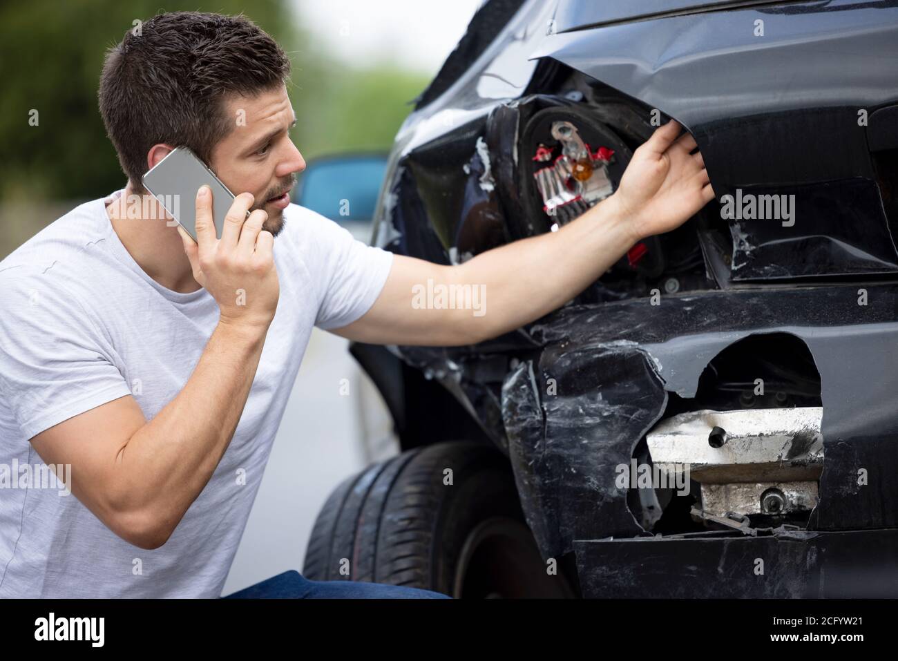 Conductor male infeliz con coche dañado después de accidente llamando al seguro Empresa en el teléfono móvil Foto de stock