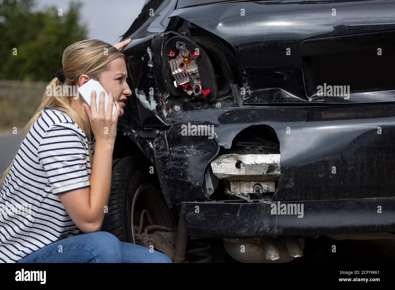 Conductor femenino infeliz con coche dañado después de accidente llamando al seguro Empresa en el teléfono móvil Foto de stock