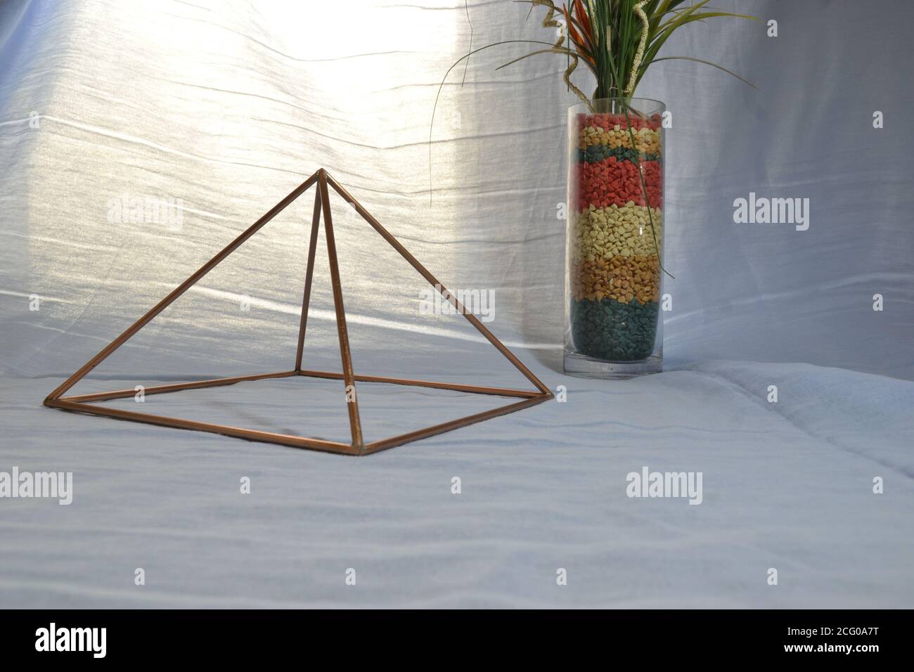 Pirámide de cobre con iluminación, con jarrón de vidrio antiguo y piedras en vista lateral, con iluminación natural de fondo, pirámide para uso doméstico Foto de stock