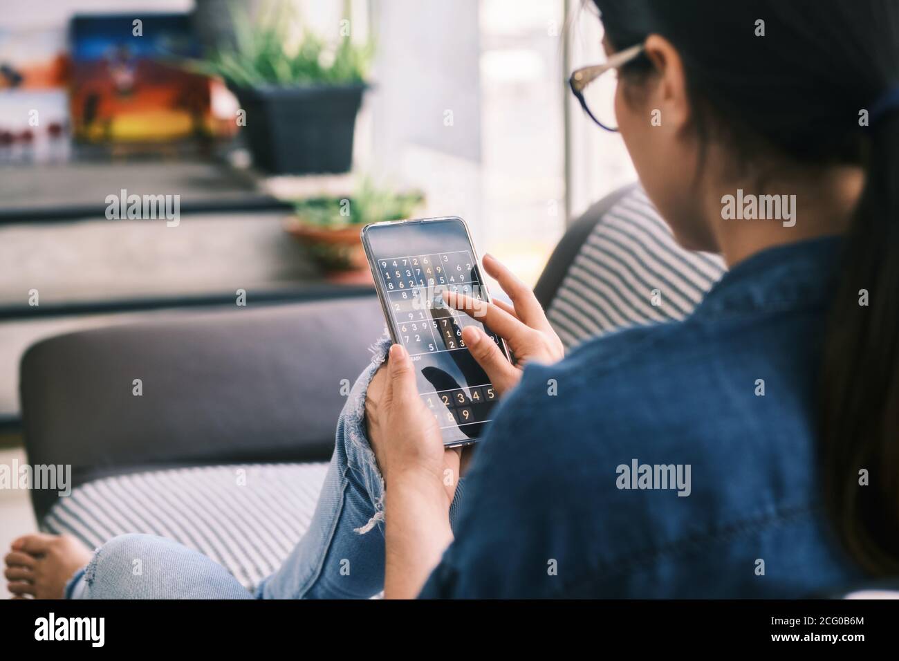 Mujer joven jugando al juego Sudoku con la aplicación en el teléfono Foto de stock
