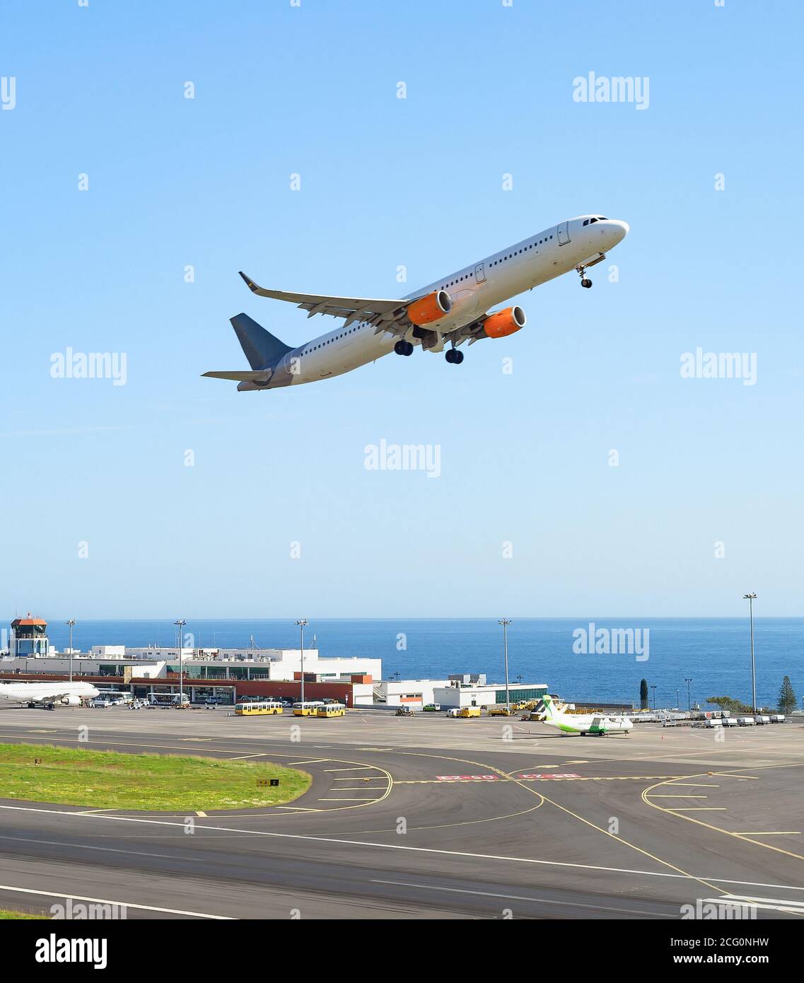 Avión despegando de la pista de aterrizaje en el aeropuerto internacional de Madeira, la construcción de la terminal y el paisaje marino en el fondo, Portugal Foto de stock