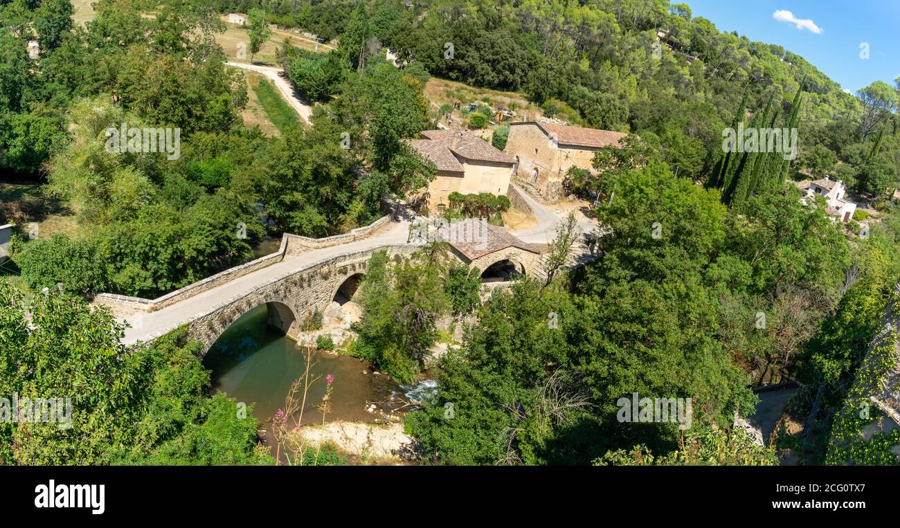 Vista panorámica de un pequeño pueblo en el sureste de Francia. Un río fluye bajo un viejo puente de piedra en un día soleado Foto de stock
