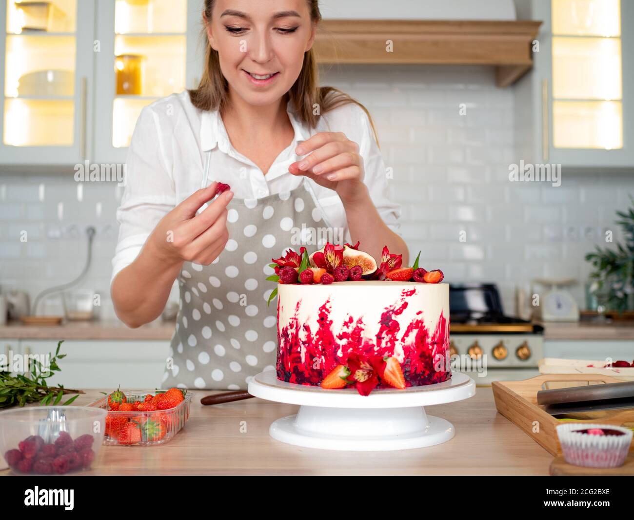 Cocina y decoración de pastel con crema. Joven chef pastelera en la cocina  decorando pastel de terciopelo rojo. Mujer feliz en delantal en la cocina  Fotografía de stock - Alamy