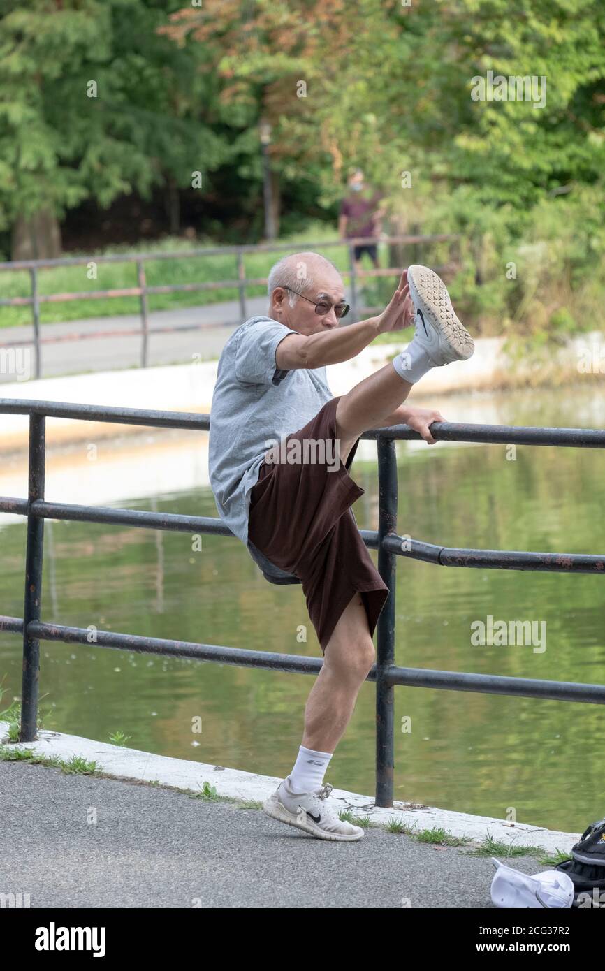 Un ciudadano adulto mayor flexible y ágil toca los dedos de los pies de una manera no convencional mientras se calienta para hacer ejercicio. En un parque en Queens, Nueva York. Foto de stock