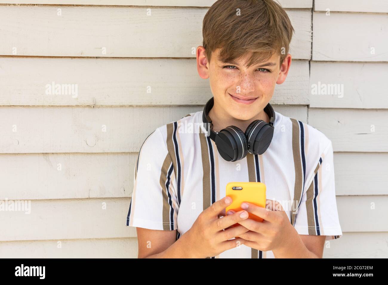 Niño adolescente adolescente niño adolescente fuera usando su célula móvil teléfono y auriculares inalámbricos blue tooth para redes sociales Foto de stock
