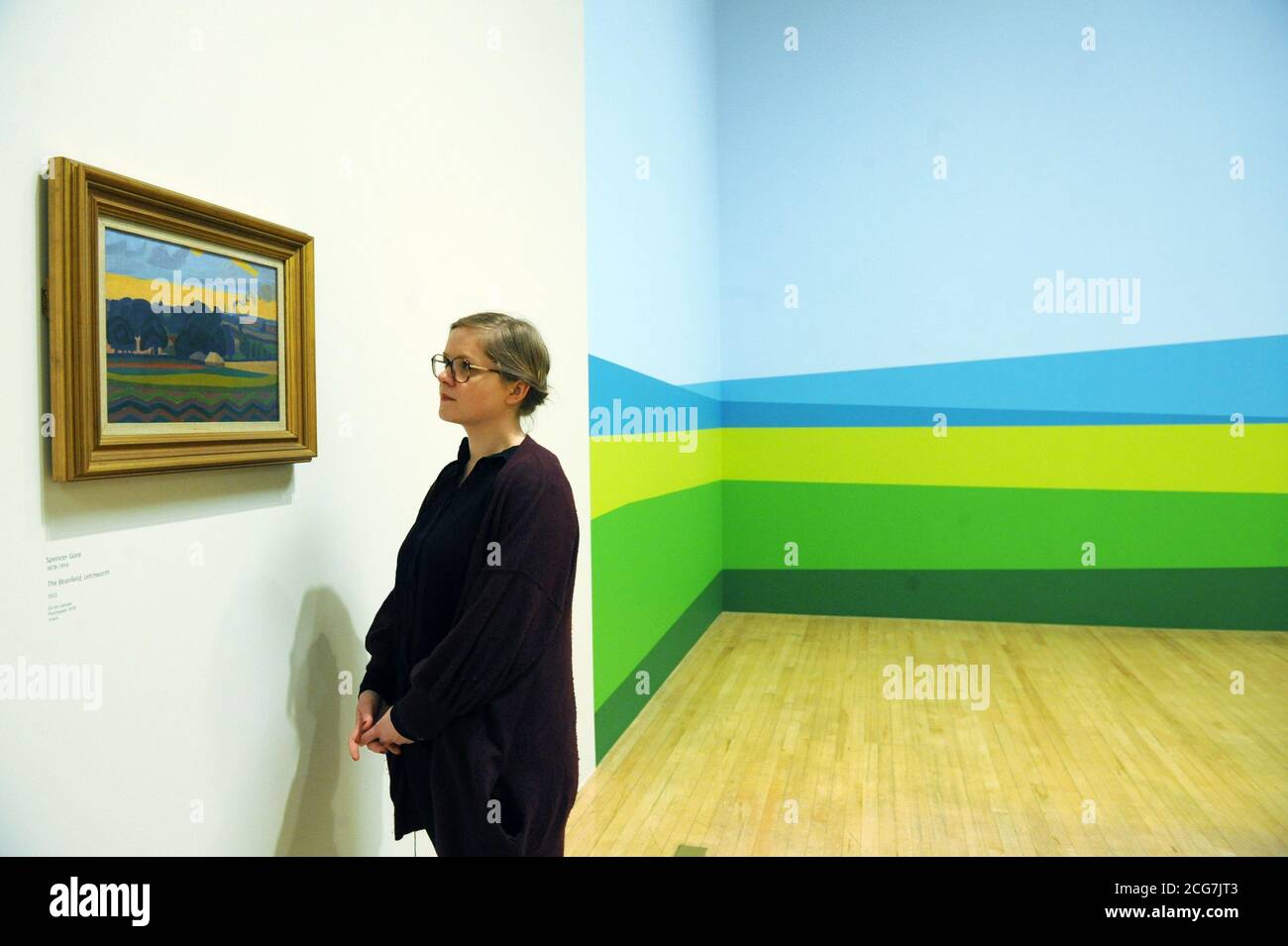 Una mujer mira el Beanfield de Spencer Gore con la gran escala de Julian Opie hay colinas en la distancia, pintado directamente en la pared de Tate Britain detrás de ella como parte de una nueva exposición en Tate Britain, Londres. Foto de stock