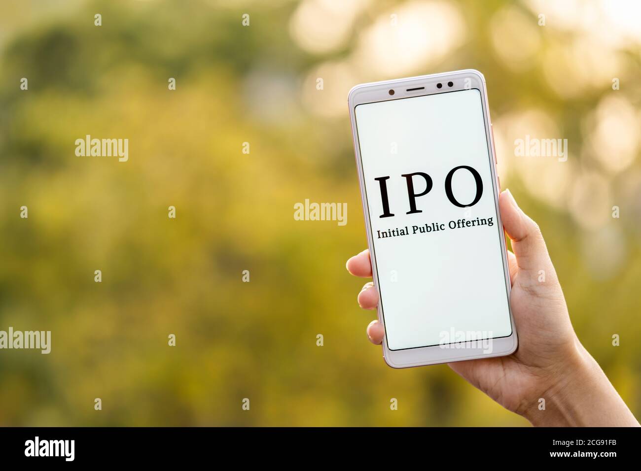 Concepto inicial de oferta pública. Joven mujer mano sosteniendo el teléfono móvil y mostrando IPO que se muestra en su pantalla en el fondo al aire libre con cop Foto de stock