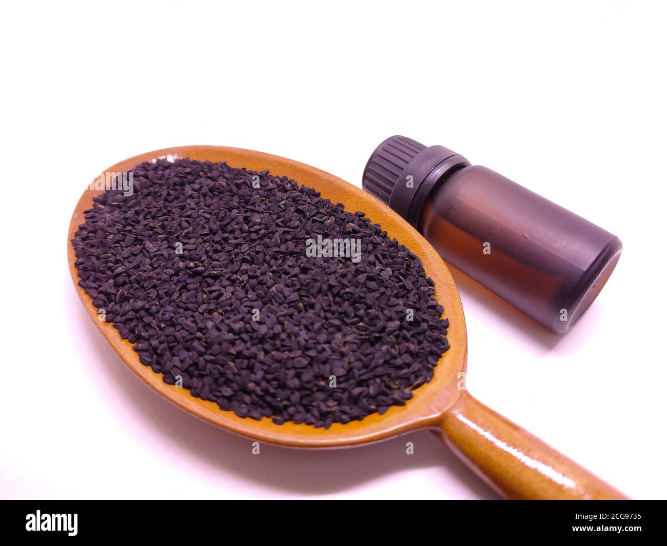 Botella de vidrio de aceite esencial de semillas de comino negro, Nigella Sativa en cuchara de madera sobre fondo blanco. Concepto de medicina herbaria Foto de stock