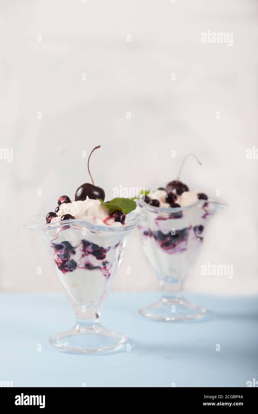 Postre de crema, grosellas y cerezas, decorado con hojas de menta sobre un plato blanco. Copiar spaes. Verticalmente. Foto de stock