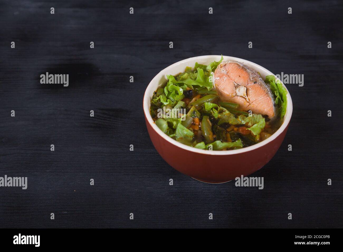 Sopa japonesa con pescado chum, judías verdes, verduras, hierbas en una taza de arcilla sobre fondo negro. Copia de espadas Foto de stock